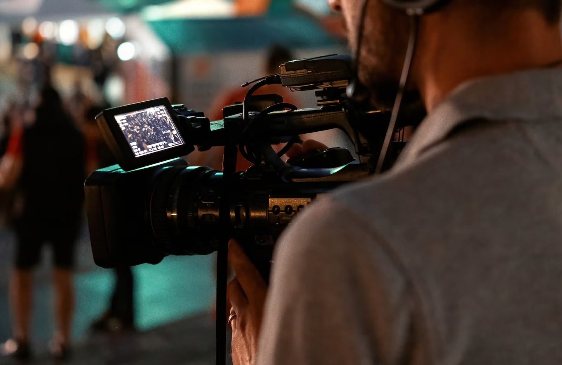 FX Productions Canada A person from FX Productions Canada operates a professional video camera outdoors at night, with the camera’s screen displaying a crowd scene in the background. Toronto Video Production Company