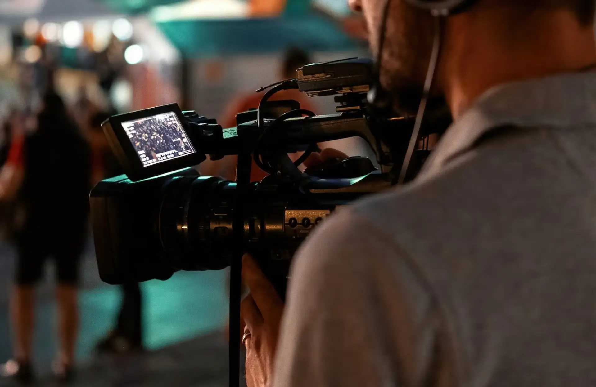 FX Productions Canada A person from FX Productions Canada operates a professional video camera outdoors at night, with the camera’s screen displaying a crowd scene in the background. Toronto Video Production Company