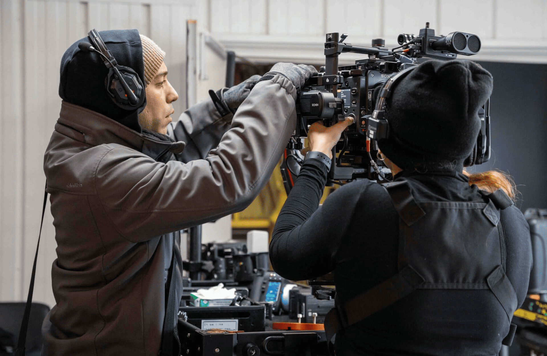 FX Productions Canada Two crew members wearing headphones and winter clothing adjust a professional video camera on set indoors, showcasing the expertise of Toronto Production Company. Toronto Video Production Company