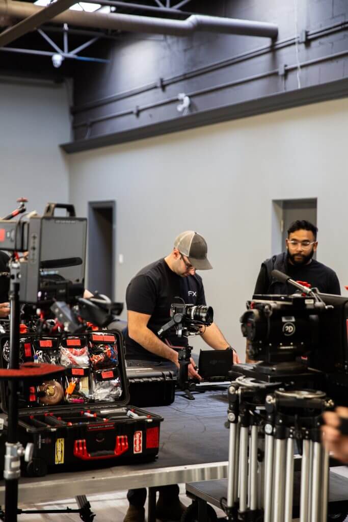 FX Productions Canada Two people set up camera equipment and gear on a table in a modern studio space with grey walls and exposed ceilings, showcasing the behind-the-scenes process at top Toronto Video Production studios. Toronto Video Production Company