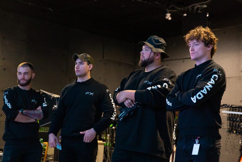 FX Productions Canada Four men wearing matching black "FX" sweatshirts stand indoors with their arms crossed, representing FX Productions Canada, a leading Toronto Video Production team, in a room filled with equipment and cables in the background. Toronto Video Production Company