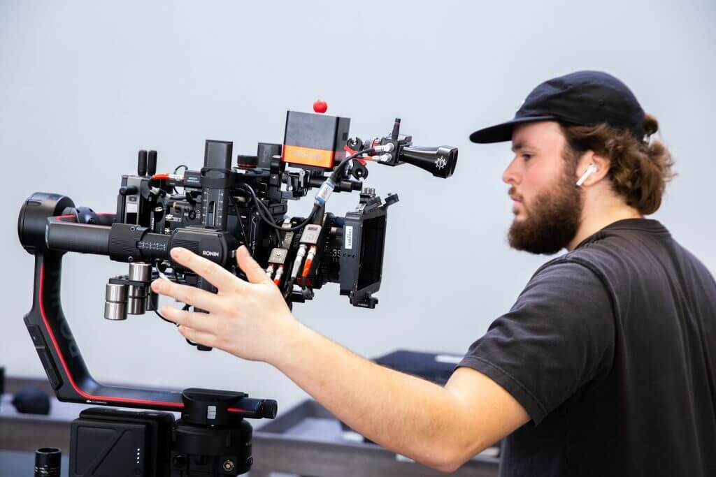 FX Productions Canada A person wearing a black cap and t-shirt operates a professional video camera mounted on a stabilizer against a plain background, showcasing the expertise of FX Productions Canada in Toronto video production. Toronto Video Production Company