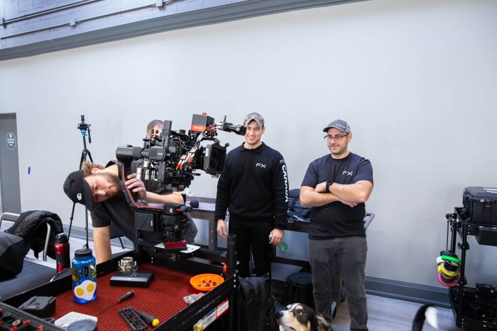 FX Productions Canada Three men stand around a film camera rig on a worktable in a studio; one adjusts the camera while the others watch. Various equipment and tools are visible on the table, showcasing the collaborative spirit of FX Productions Canada, a leading Toronto Video Production team. Toronto Video Production Company