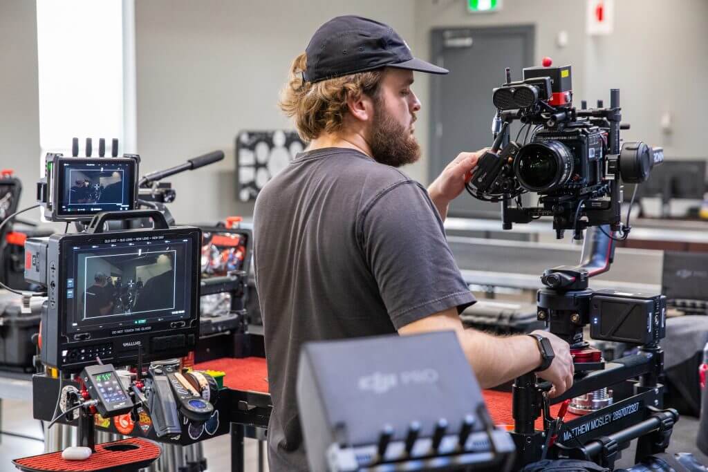 FX Productions Canada A man in a black shirt and cap operates a professional video camera on set for FX Productions Canada, surrounded by monitors and film equipment at this Toronto Video Production. Toronto Video Production Company