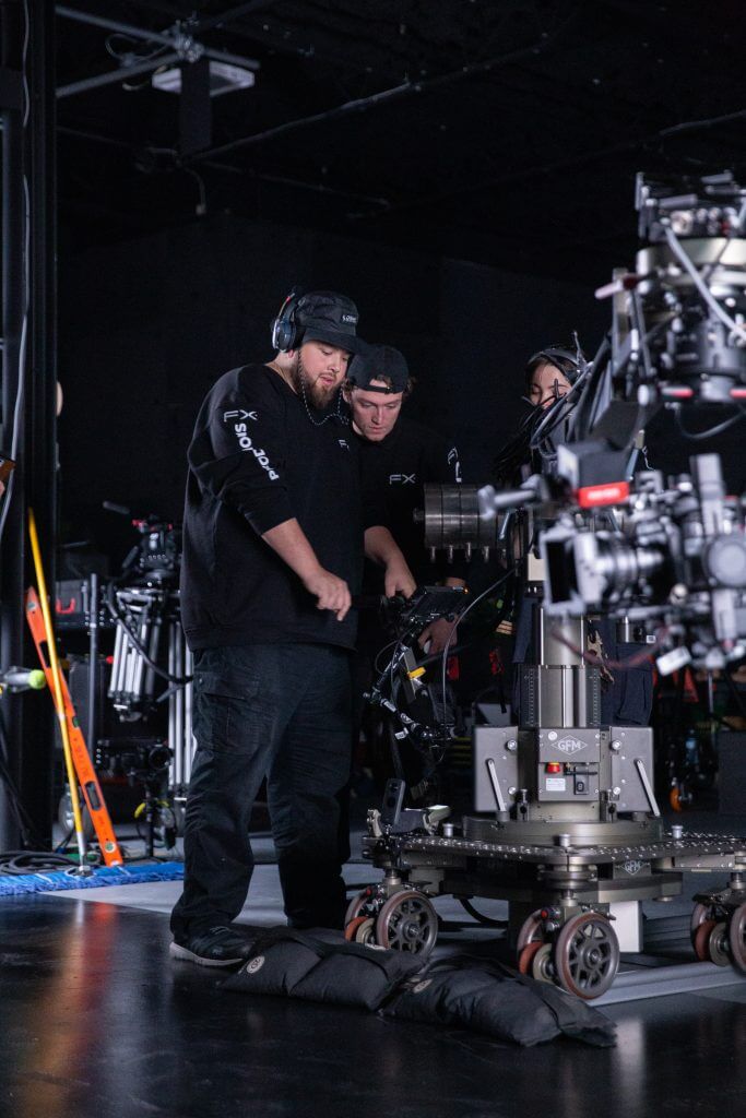 FX Productions Canada Two crew members operate a camera dolly on a film set surrounded by equipment in a dimly lit studio at FX Productions Canada, a leading Toronto Video Production company. Toronto Video Production Company