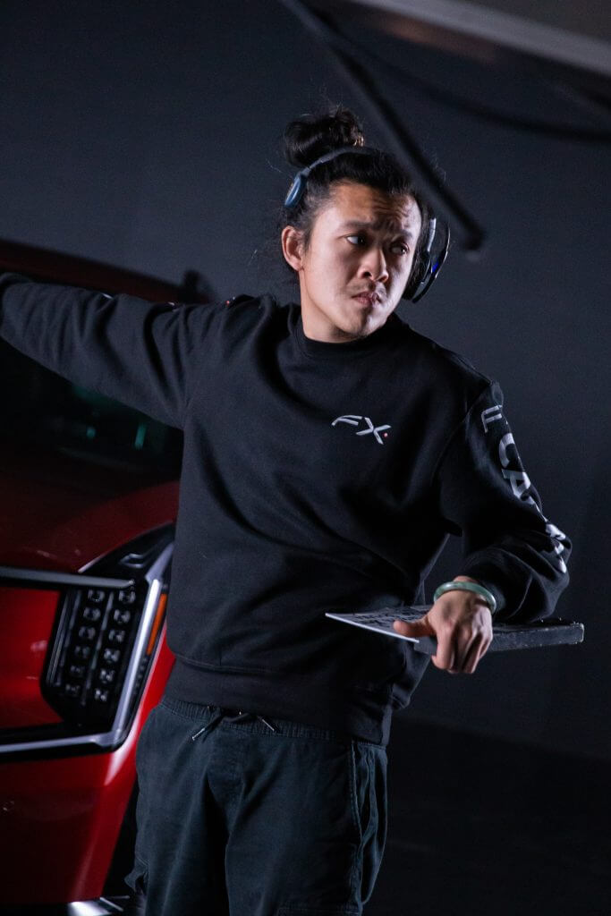 FX Productions Canada A person wearing headphones and a black sweatshirt stands beside a red vehicle, holding a clipboard and gesturing with one arm—capturing the behind-the-scenes action of Toronto Video Production. Toronto Video Production Company