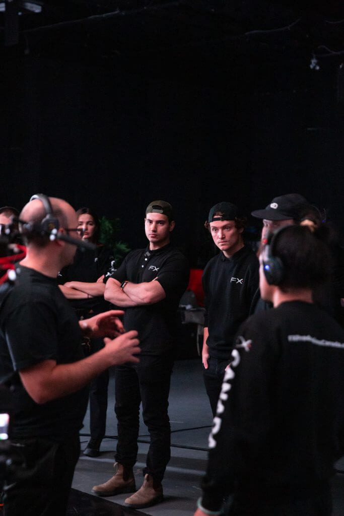 FX Productions Canada A group of people in black shirts stand indoors, listening attentively to a person from FX Productions Canada speaking and gesturing with their hands. Some wear headsets. Toronto Video Production Company