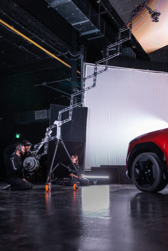 FX Productions Canada Two people from FX Productions Canada operate film equipment and a camera crane on a studio set next to a red vehicle, with a white backdrop in the background. Toronto Video Production Company