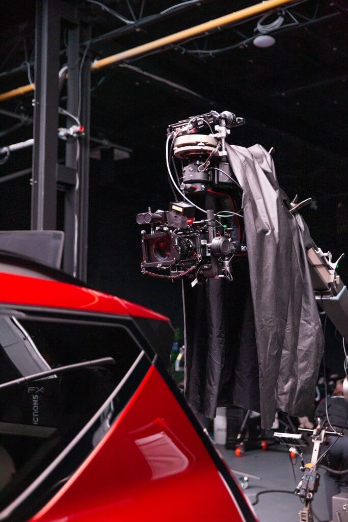 FX Productions Canada A robotic camera rig covered in a black cloth is positioned next to a red car inside a dimly lit studio, capturing behind-the-scenes footage for Toronto Video Production. Toronto Video Production Company