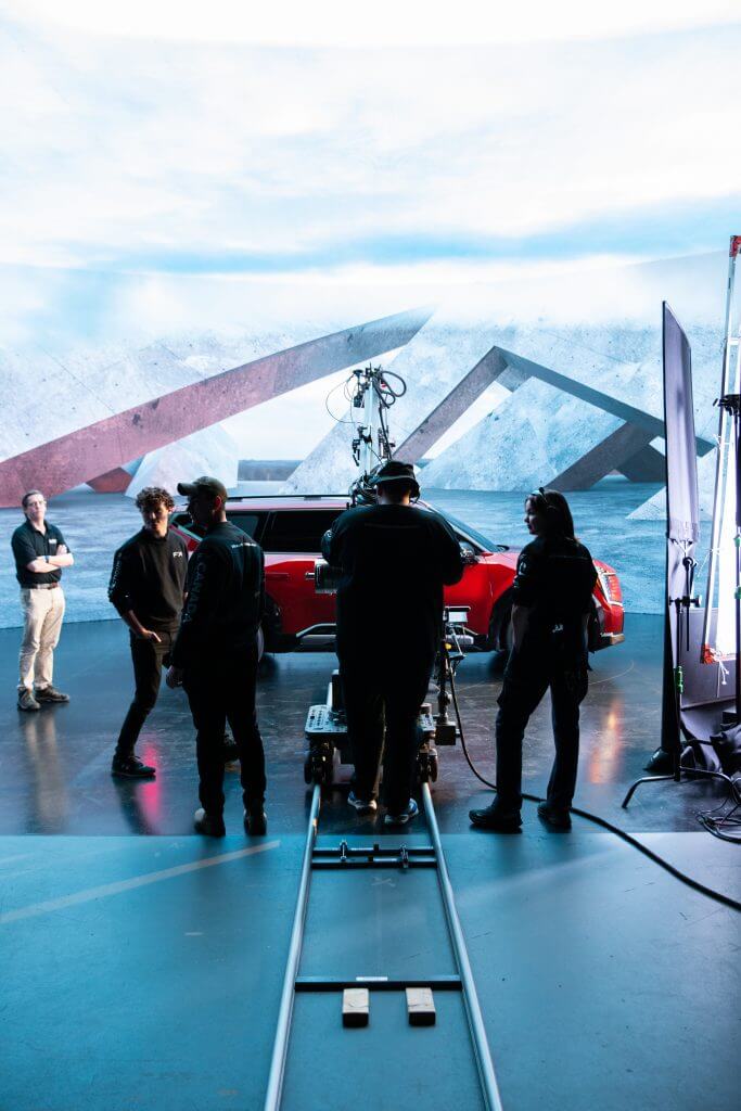 FX Productions Canada Crew on a film set stand near a camera dolly track, with a red car and geometric backdrop in the background—a glimpse behind the scenes at Toronto Video Production excellence. Toronto Video Production Company