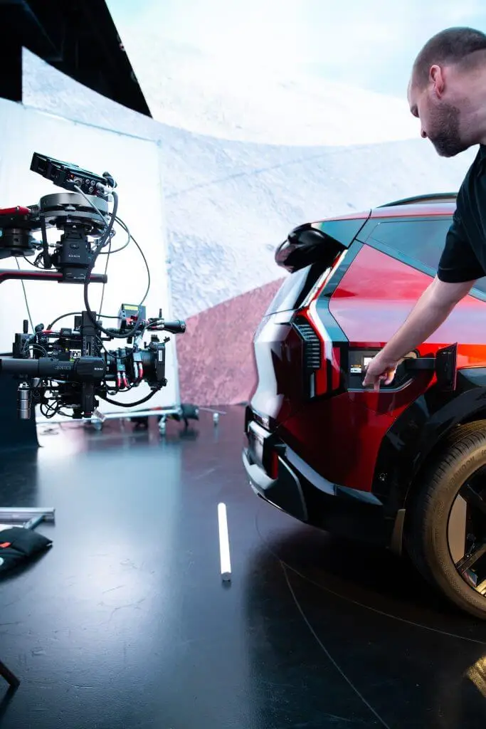 FX Productions Canada A person points at the charging port of a red electric vehicle while a Toronto Video Production company films nearby in a studio setting. Toronto Video Production Company