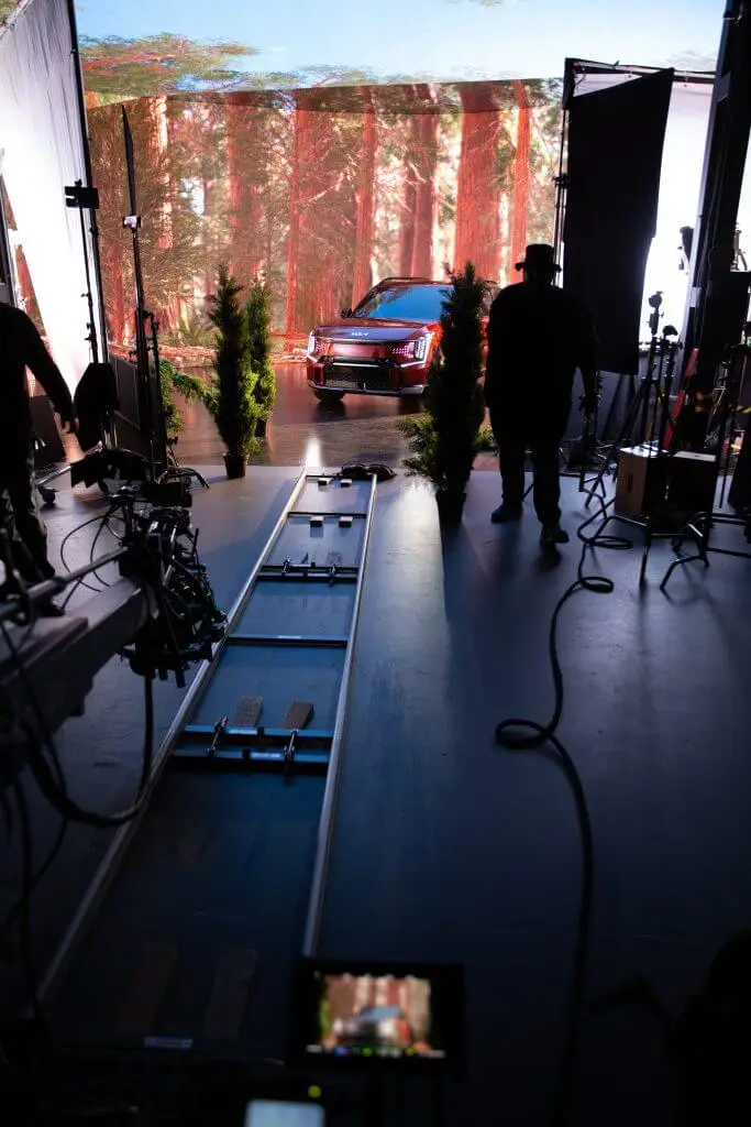FX Productions Canada A studio setup by Toronto Video Production features camera tracks and filming equipment aimed at a car parked before a forest backdrop, with crew members from the video production company standing nearby. Toronto Video Production Company