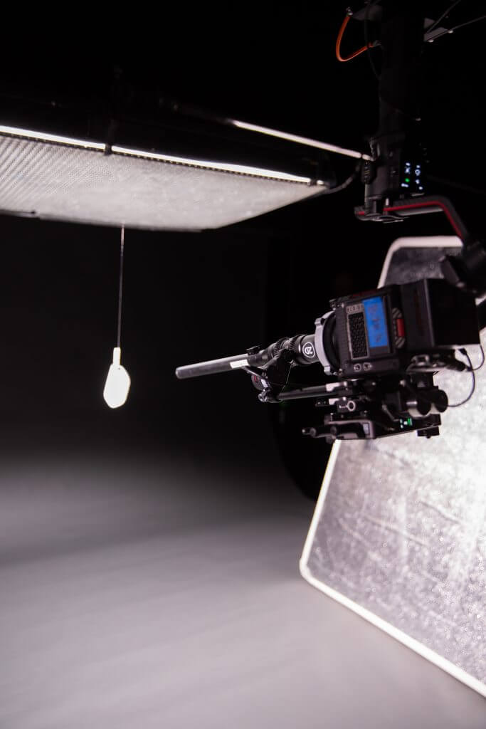 FX Productions Canada A professional camera is set up in a studio by Toronto Video Production experts, aimed at a hanging lightbulb with a diffuser and reflector positioned nearby. Toronto Video Production Company