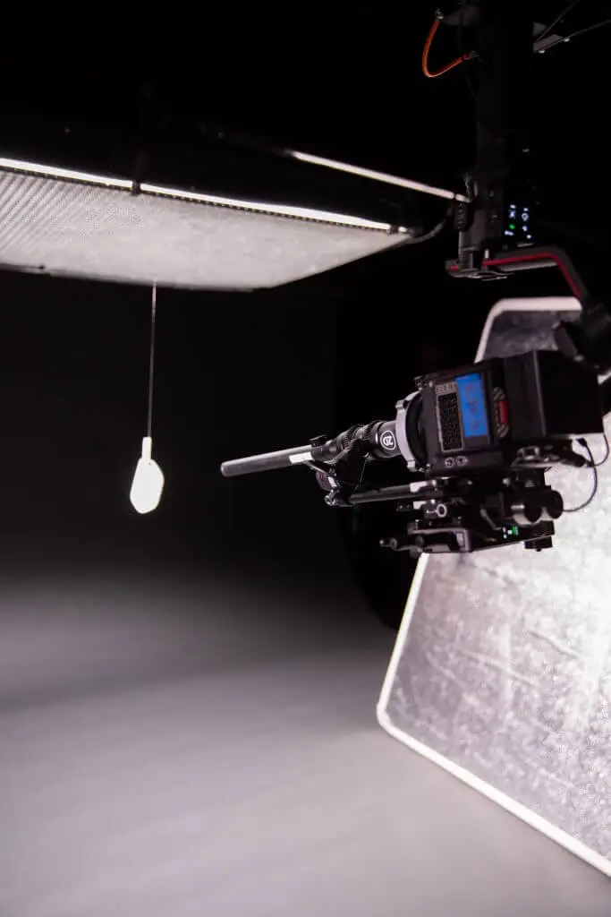 FX Productions Canada A professional camera is set up in a studio by Toronto Video Production experts, aimed at a hanging lightbulb with a diffuser and reflector positioned nearby. Toronto Video Production Company
