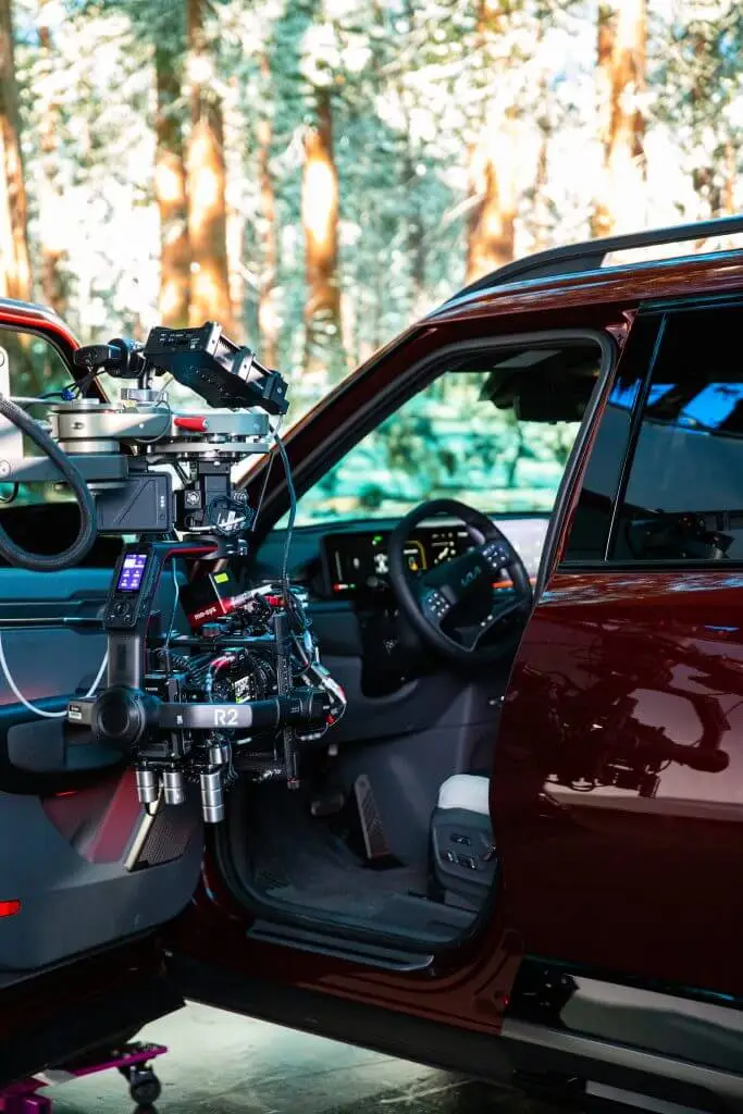 FX Productions Canada A professional camera rig from a Toronto Video Production company is mounted outside the open driver's door of a maroon vehicle, capturing the interior with a forest visible in the background. Toronto Video Production Company