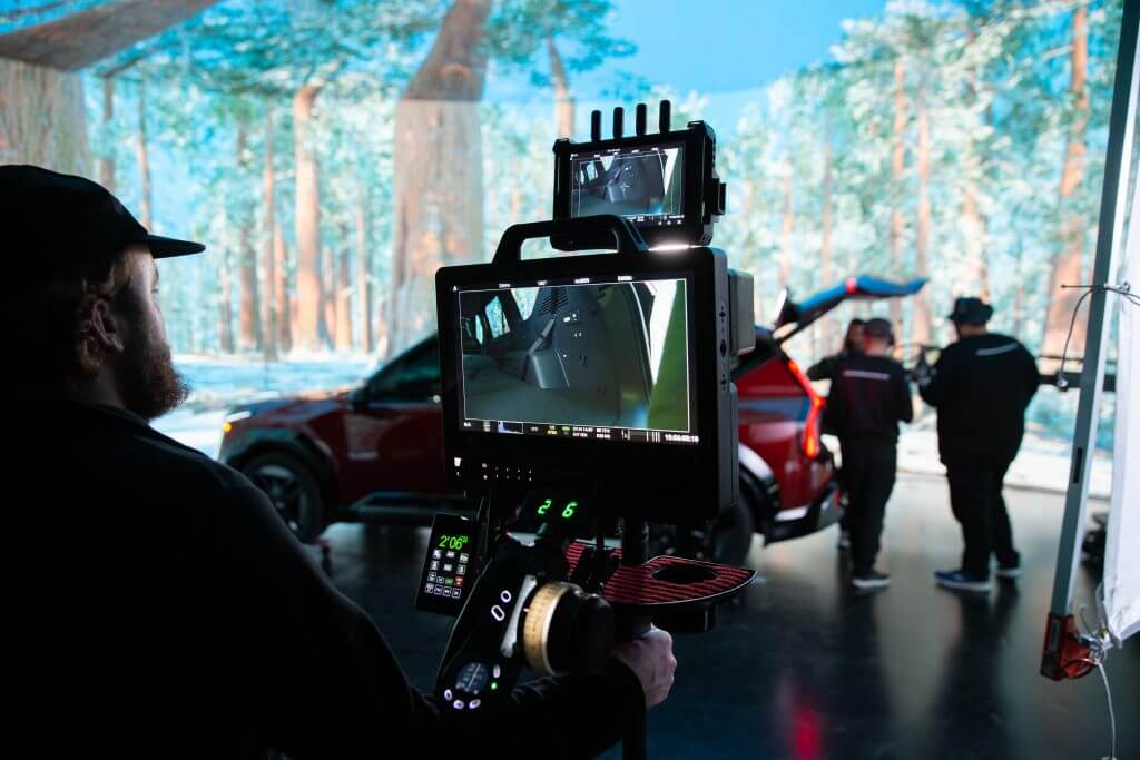 FX Productions Canada A person operates a camera rig displaying a car’s interior while two people stand near an SUV with open doors, all inside a studio set with a forest backdrop at FX Productions Canada, a leading Toronto Video Production company. Toronto Video Production Company
