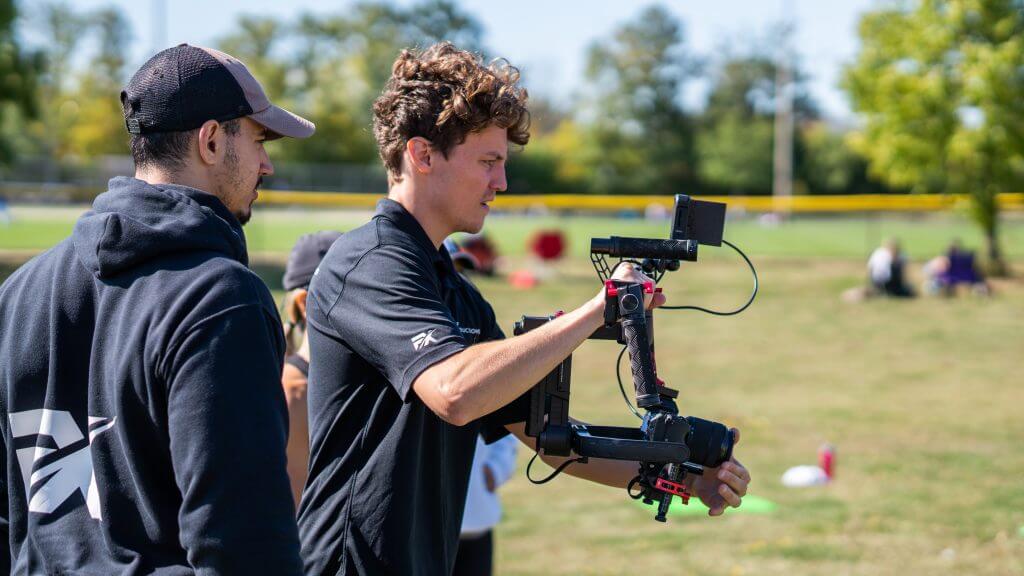 FX Productions Canada Two men outdoors operate a handheld video camera rig with a monitor, standing on grass with blurred people and trees in the background—capturing the moment for FX Productions Canada, a leading Toronto Video Production company. Toronto Video Production Company