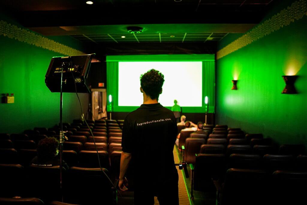 FX Productions Canada A person stands in the aisle of a dimly lit theater with green lighting, facing a screen at the front while a few others are seated—captured by FX Productions Canada, a leading Toronto Video Production company. Toronto Video Production Company