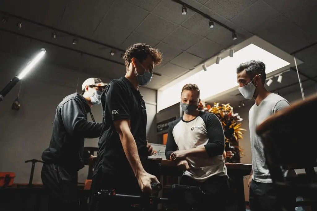 FX Productions Canada Four men wearing face masks stand together indoors, engaged in conversation around a table under bright ceiling lights at FX Productions Canada, a leading Toronto Video Production company. Toronto Video Production Company