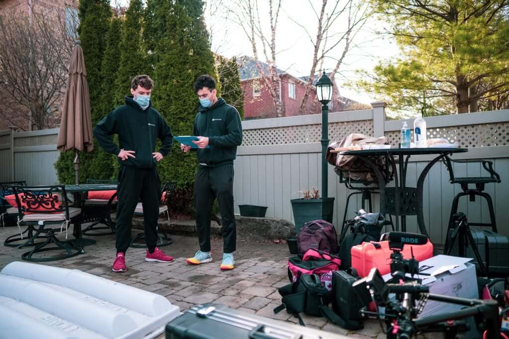 FX Productions Canada Two people wearing masks stand in a backyard near a table and various equipment, including bags and a camera—capturing the behind-the-scenes work of a Toronto Video Production company, with outdoor furniture and trees in the background. Toronto Video Production Company