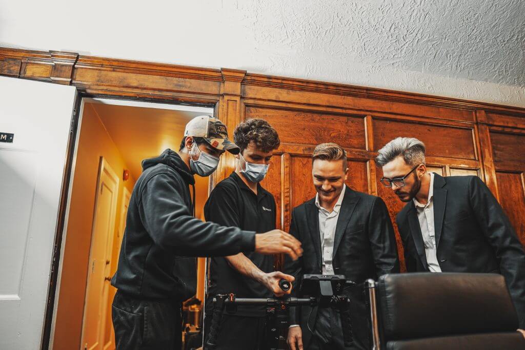 FX Productions Canada Four men, two in suits and two in casual clothes, stand together looking at camera equipment in an office with wood-paneled walls at FX Productions Canada, a leading Toronto Video Production company. Toronto Video Production Company
