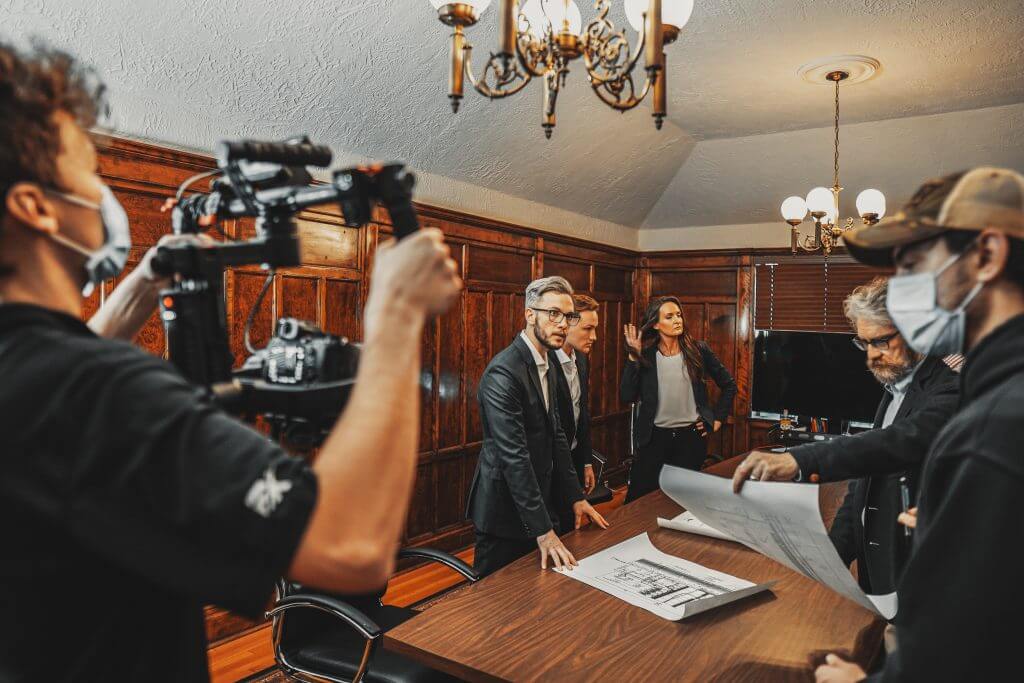 FX Productions Canada A film crew from FX Productions Canada records a scene with people in business attire gathered around a table reviewing blueprints in a wood-paneled meeting room. Toronto Video Production Company