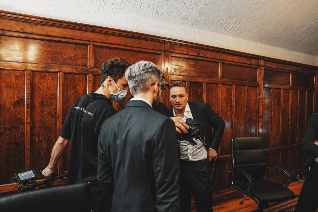 FX Productions Canada Four men in suits and business attire gather around a camera setup in a wood-paneled room, reviewing the display—a behind-the-scenes look at FX Productions Canada, a leading Toronto Video Production company. Toronto Video Production Company