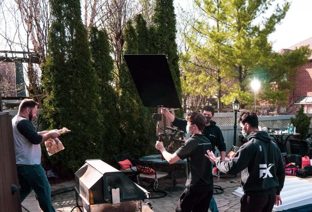 FX Productions Canada A film crew from FX Productions Canada records a man holding food near an outdoor grill; trees and patio furniture are visible in the background. Toronto Video Production Company