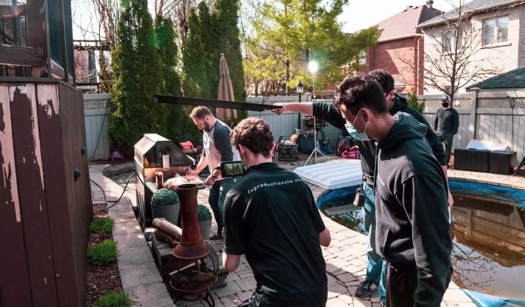 FX Productions Canada Four people set up film equipment in a backyard near a pool, preparing for a shoot on a sunny day with FX Productions Canada, a leading Toronto Video Production company. Toronto Video Production Company