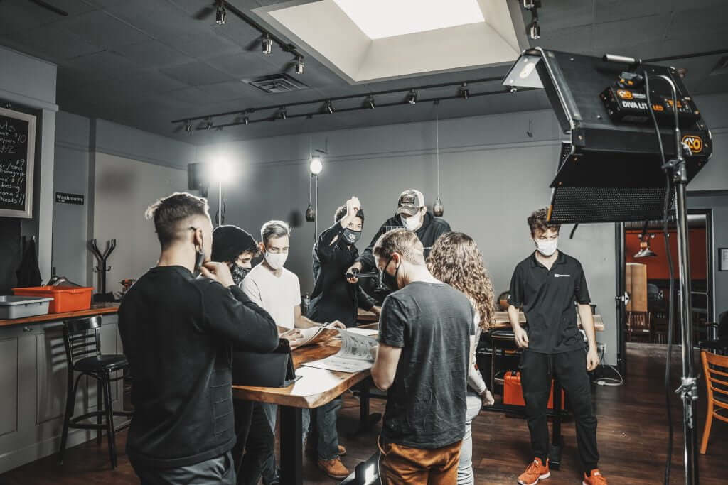 FX Productions Canada A group of people wearing masks and casual clothes work together on a film set, surrounded by cameras, lights, and equipment in an indoor studio at FX Productions Canada. Toronto Video Production Company