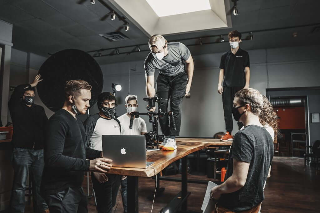FX Productions Canada A film crew, all wearing masks, collaborates around a table with a camera rig and laptop in a studio under bright lighting—showcasing the expertise of FX Productions Canada, a leading Toronto Video Production company. Toronto Video Production Company