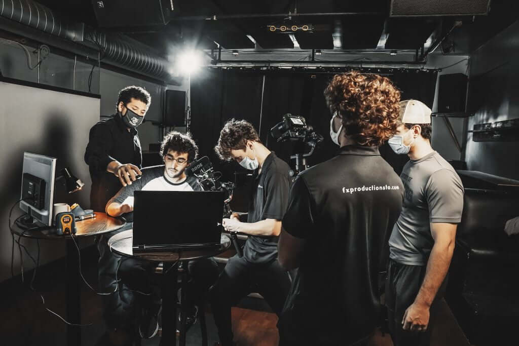 FX Productions Canada Five people wearing masks work with a laptop and camera equipment in a dimly lit room, highlighting a Toronto Video Production team on set. Toronto Video Production Company