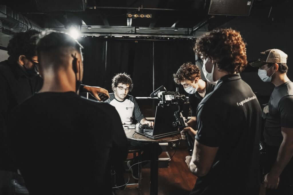 FX Productions Canada A group of people, some wearing masks, film a man sitting at a table with a laptop and microphones in a dimly lit room for FX Productions Canada. Toronto Video Production Company