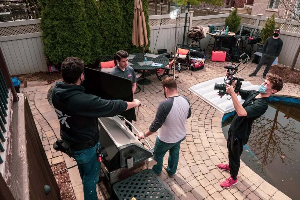 FX Productions Canada Four people are filming a scene by a backyard grill near a small pool, with camera equipment and bags scattered around the patio—a typical shoot for a Toronto Video Production team. Toronto Video Production Company