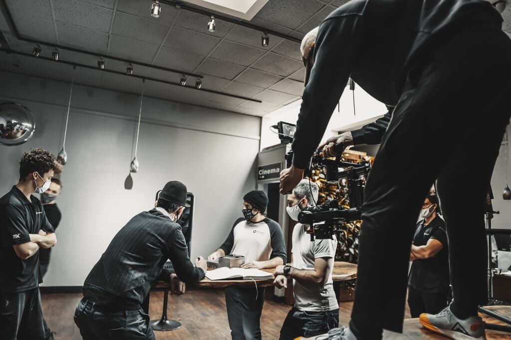 FX Productions Canada A Toronto Video Production crew, wearing masks, arranges equipment and discusses around a table in a studio, with one person operating a camera rig elevated above them. Toronto Video Production Company