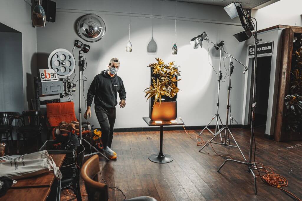 FX Productions Canada A person wearing a mask stands in a studio setup by FX Productions Canada, with professional lighting equipment focused on a table with a potted plant. Toronto Video Production Company