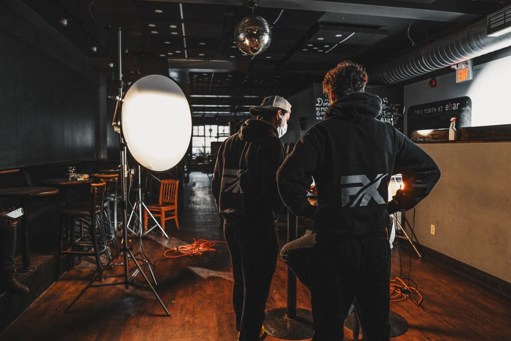 FX Productions Canada Two people in matching hoodies stand in a dimly lit room with professional lighting and filming equipment set up, showcasing the creative process at this Toronto Video Production company. Toronto Video Production Company