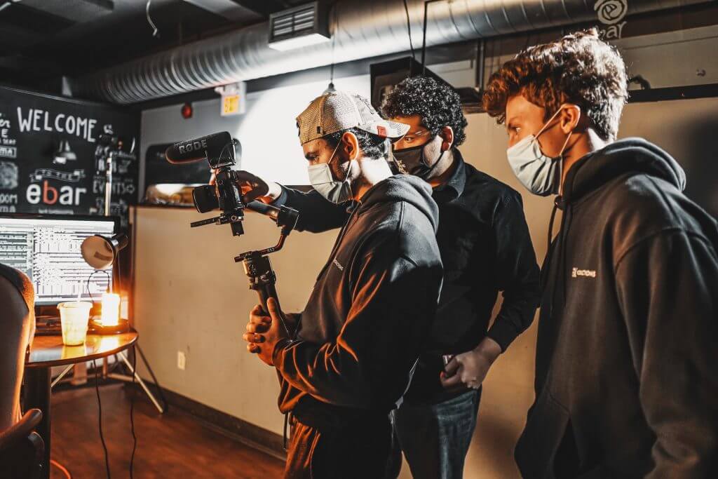 FX Productions Canada Three people wearing face masks operate a camera and film equipment indoors, focusing on the camera’s screen—capturing the creative spirit of FX Productions Canada, a leading Toronto Video Production company. Toronto Video Production Company