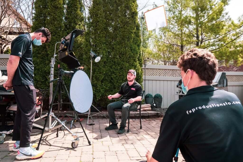 FX Productions Canada Three people set up a video shoot outdoors with lighting equipment, reflectors, and cameras; one person is seated while the others adjust equipment for FX Productions Canada, a leading Toronto Video Production company. Toronto Video Production Company