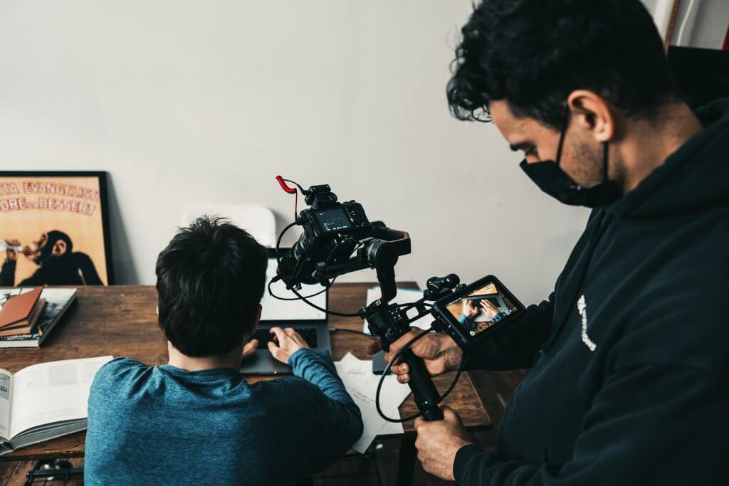 FX Productions Canada A person types at a desk with books and papers while another, from FX Productions Canada, films them using a camera on a stabilizer. Toronto Video Production Company