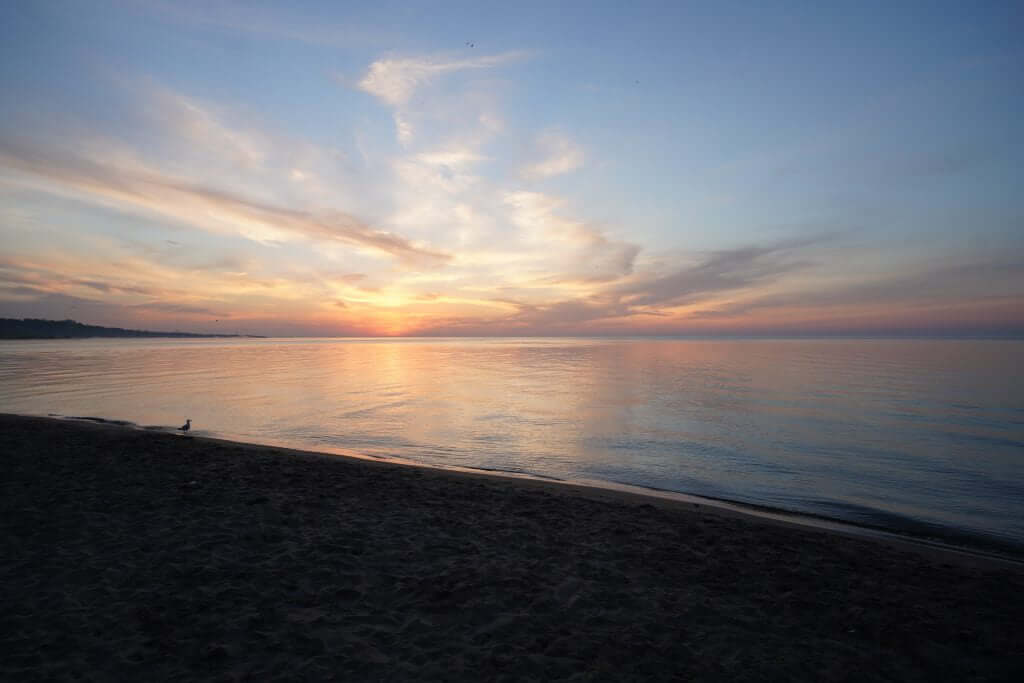 FX Productions Canada A calm beach at sunset with soft orange and blue tones in the sky, reflecting on the water, and a dark sandy shoreline in the foreground—perfect inspiration for any Toronto Video Production seeking serene visuals. Toronto Video Production Company