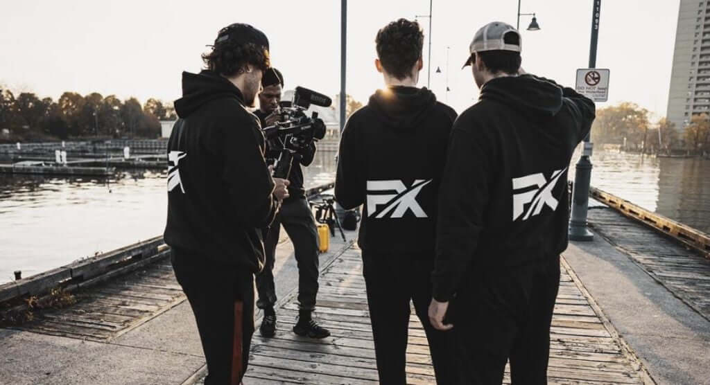 FX Productions Canada Four people stand on a dock; one operates a camera while the others, wearing matching FX Productions Canada hoodies, face the water. Toronto Video Production Company