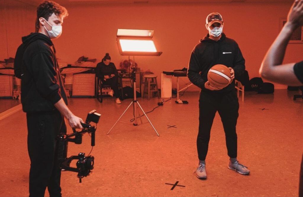 FX Productions Canada Two people wearing masks stand in a studio; one holds a camera rig, the other a basketball. A bright light and equipment are in the background—capturing creative moments at FX Productions Canada, a leading Toronto video production company. Toronto Video Production Company