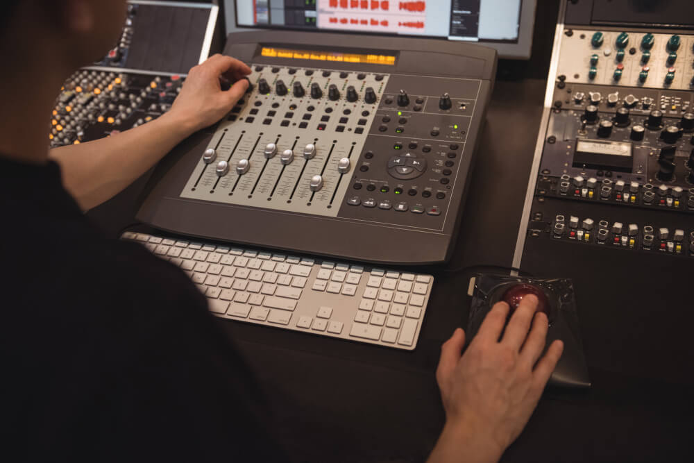 FX Productions Canada A person operates an audio mixing console and a trackball mouse at a workstation filled with audio equipment and a computer keyboard, showcasing the behind-the-scenes expertise at FX Productions Canada, a leading Toronto Video Production company. Toronto Video Production Company