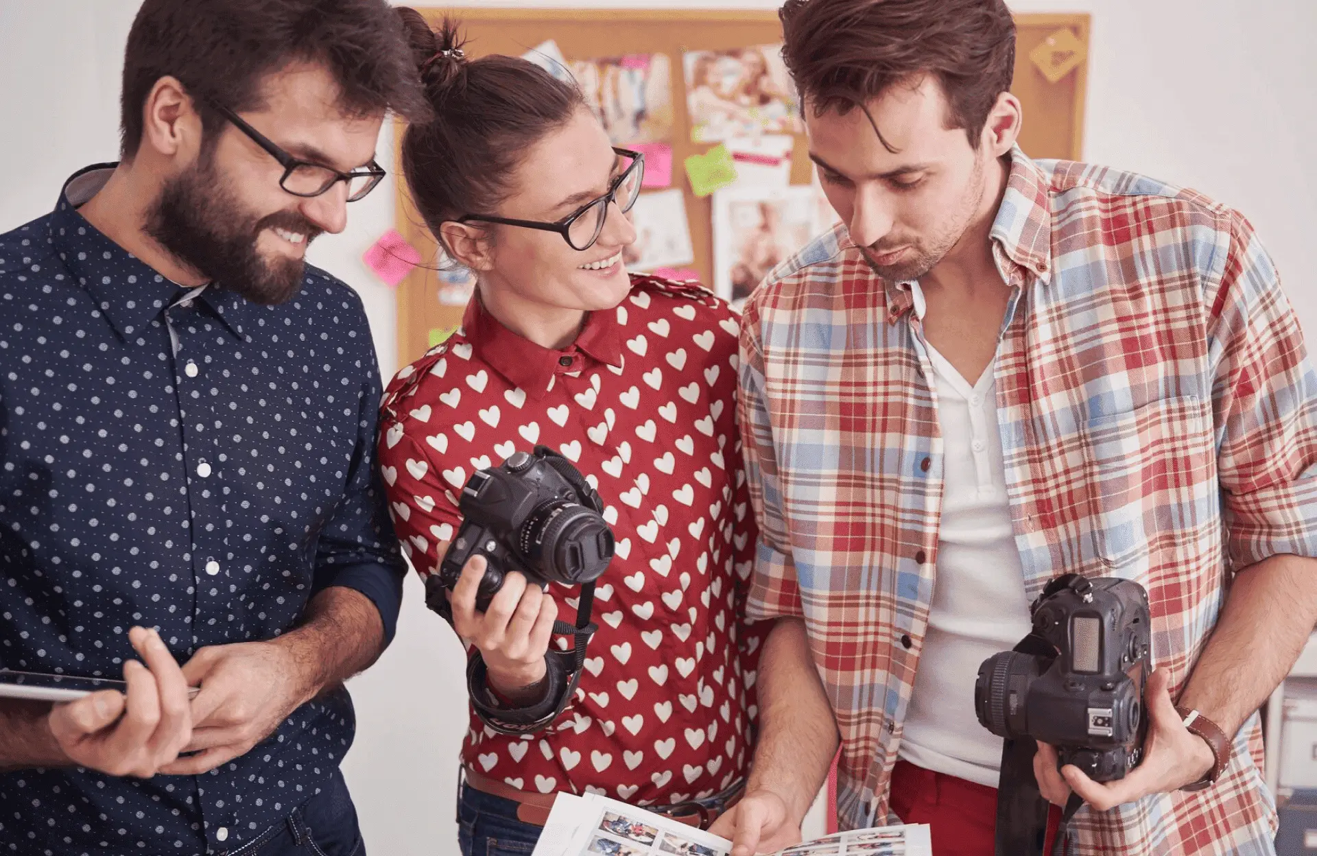 FX Productions Canada Three people stand together in an office, holding cameras and looking at printed photos, with a corkboard visible in the background—a glimpse behind the scenes at Toronto Production Company. Toronto Video Production Company