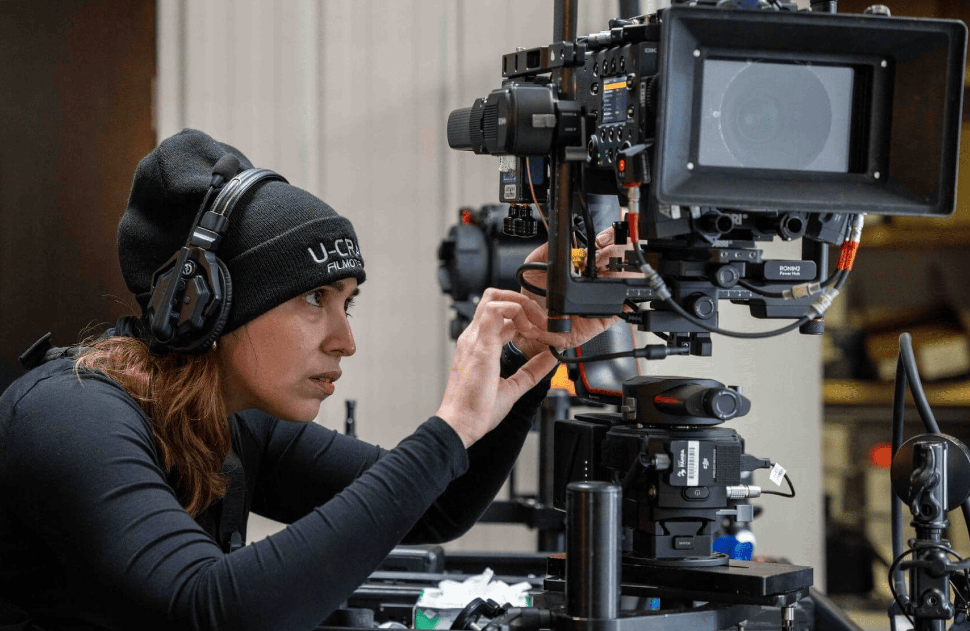 FX Productions Canada A person wearing headphones and a beanie adjusts a professional video camera mounted on a tripod indoors, showcasing the behind-the-scenes work of FX Productions Canada. Toronto Video Production Company