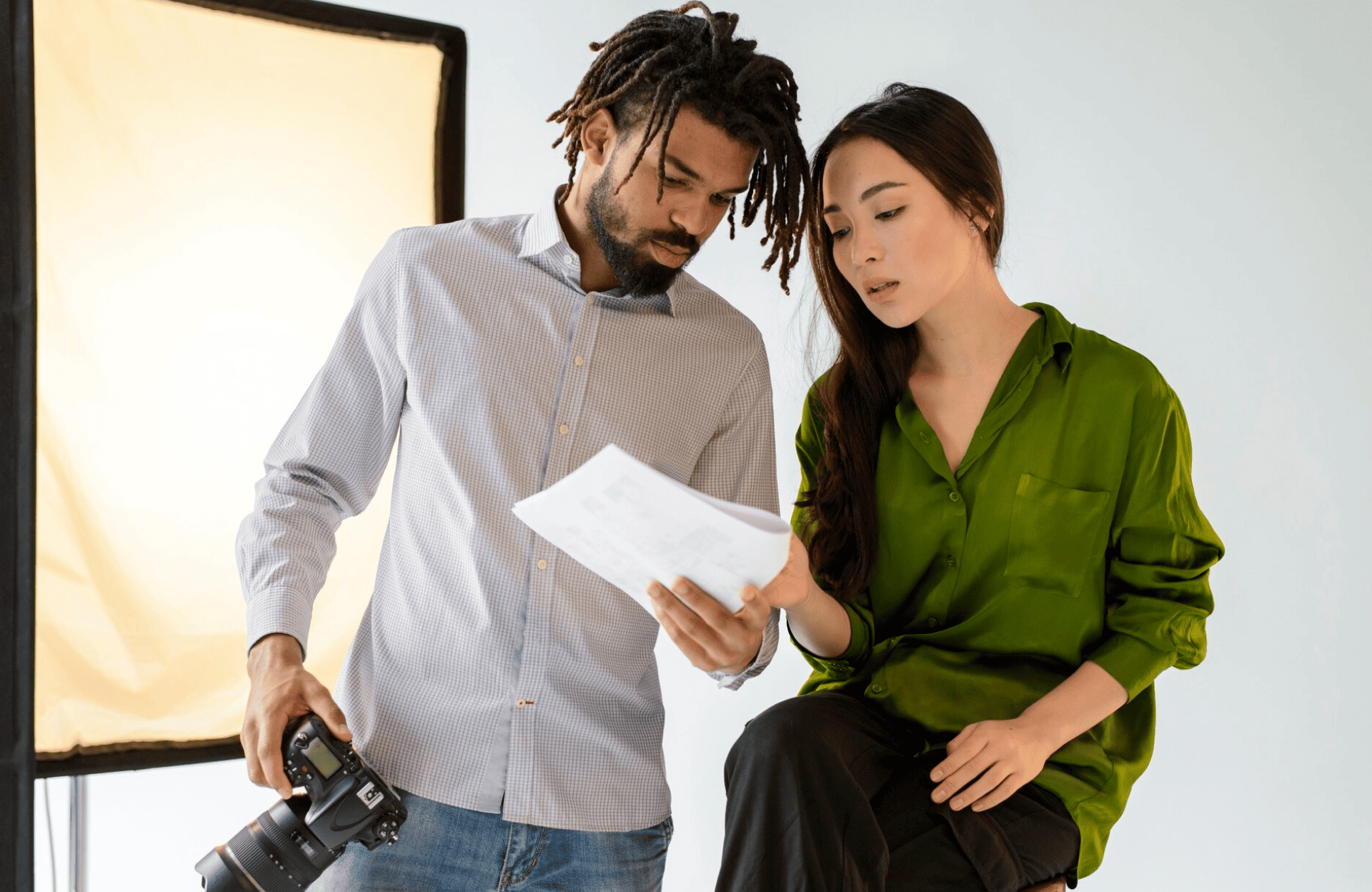 FX Productions Canada A man holding a camera and a woman in a green shirt look at a document together in a well-lit studio, showcasing the collaborative spirit of FX Productions Canada. Toronto Video Production Company