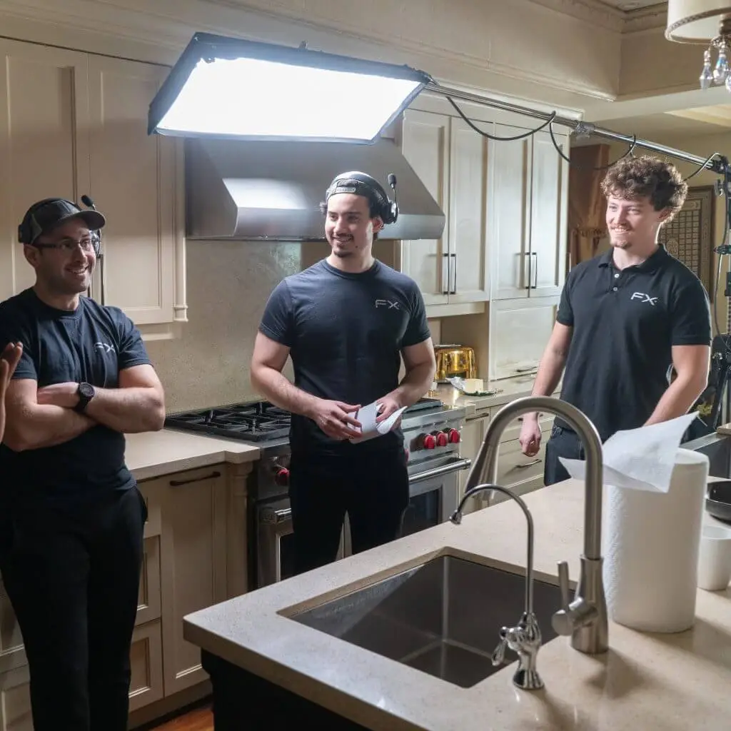 FX Productions Canada Three men in black shirts stand and talk in a kitchen set, surrounded by professional lighting equipment and filming gear from Toronto Video Production experts. Toronto Video Production Company