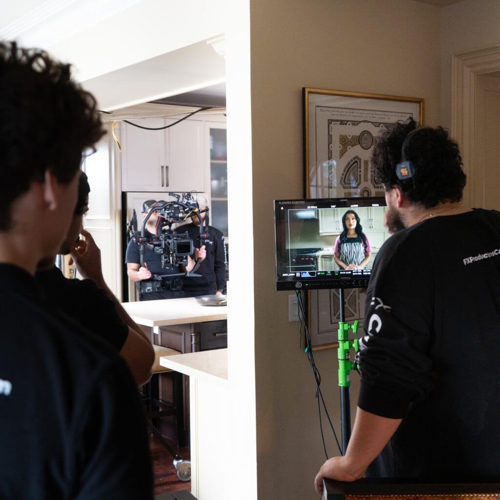 FX Productions Canada A film crew from FX Productions Canada records a woman standing in a kitchen, while a crew member of the Toronto Video Production team monitors the scene on a screen in the foreground. Toronto Video Production Company