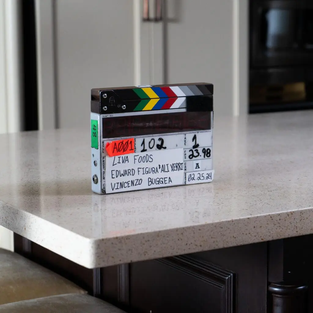 FX Productions Canada A film clapperboard labeled "LIVA FOODS" rests on a kitchen counter, displaying production details and dated 02.25.24, showcasing the work of a leading Toronto Video Production company. Toronto Video Production Company